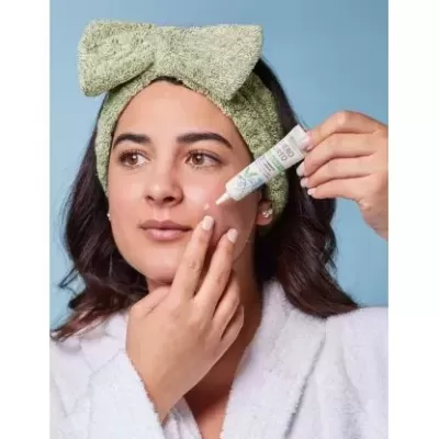 Mulher com faixa verde felpuda aplica creme facial com embalagem tubular branca