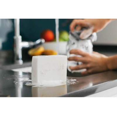 Sabão branco ensaboado numa bancada de cozinha com mãos a segurarem embalagem branca em fundo desfocado