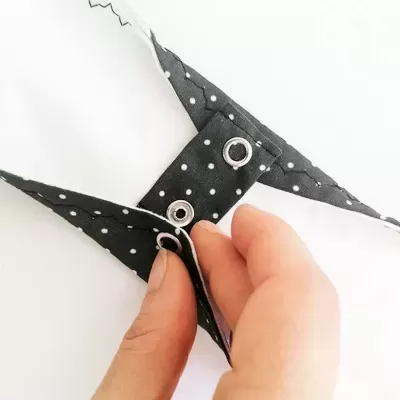 Peça de tecido preta com bolinhas brancas e ilhós metálicos