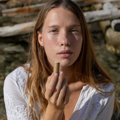 Mulher segura batom bege claro em embalagem ecológica com fundo natural