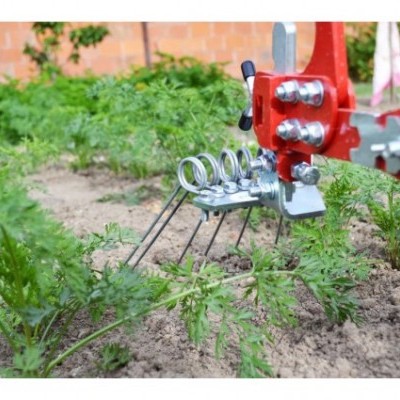 Ferramenta agrícola vermelha com molas metálicas e parafusos em jardim com plantas e muro de tijolos