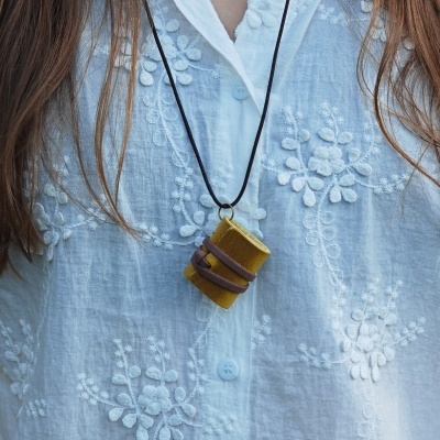 Colar com pendente de livro amarelo e castanho sobre camisa branca bordada