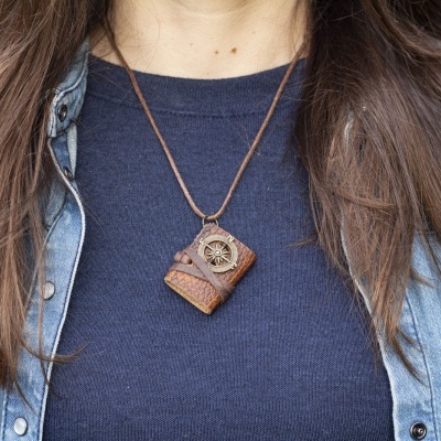 Colar em forma de livro em couro castanho sobre camiseta azul escura e camisa de ganga azul clara