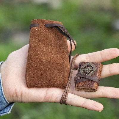 mão segurando saco de camurça castanha e objeto de madeira com bússola