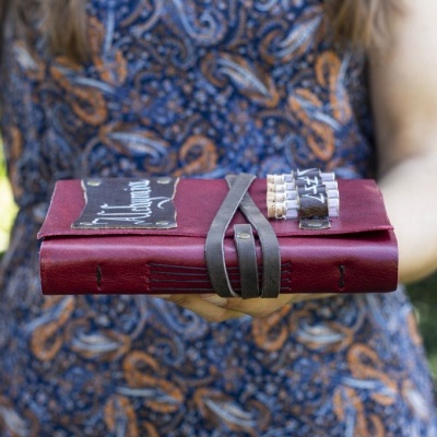 Diário de capa vermelha em couro com fecho segurado por mulher com vestido azul com padrão laranja