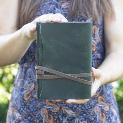 Caderno de capa verde com tira castanha segurado por pessoa com vestido azul com padrão laranja