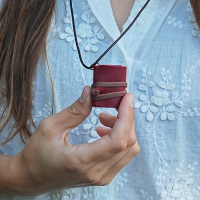 Caderno pequeno vermelho com capa de couro pendurado num cordão preto ao pescoço