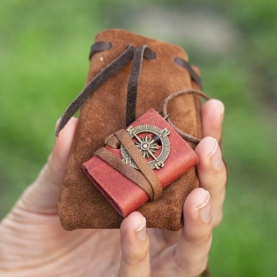 Mão segurando saco de camurça castanha e pequeno diário vermelho decorado