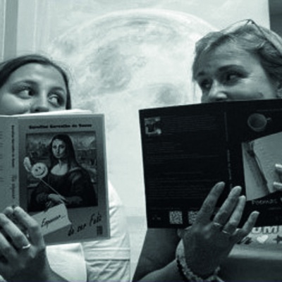 Duas mulheres segurando livros, uma capa com Mona Lisa segura uma máscara sorridente.