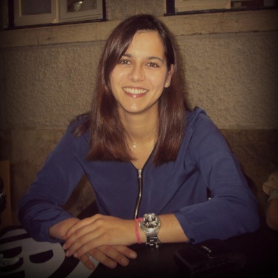 Mulher sentada com casaco azul escuro e relógio de pulso prateado num ambiente interior