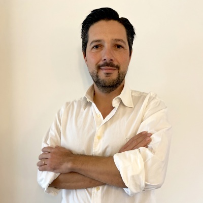 Homem de camisa branca com braços cruzados e fundo branco.