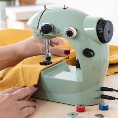 Máquina de costura portátil verde azul em tecido amarelo com bobinas de linha