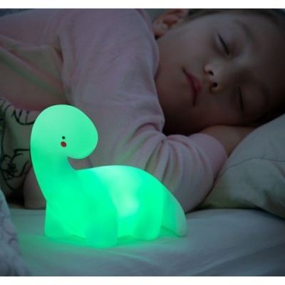 Luz noturna dinossauro verde ao lado de criança adormecida na cama