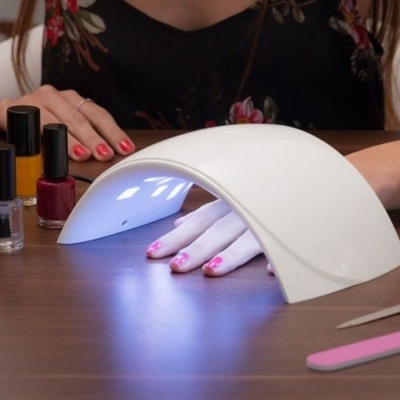 Dispositivo branco de secagem de unhas UV com mão feminina e vernizes coloridos