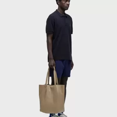 Homem com polo preta, calções azuis e bolsa bege em couro