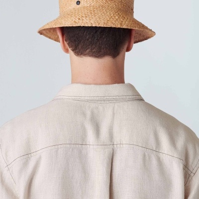 Homem de costas com chapéu bucket de palha castanha clara e camisa bege claro