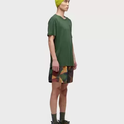 Homem com gorro amarelo esverdeado, t-shirt verde, calções coloridos e ténis castanho