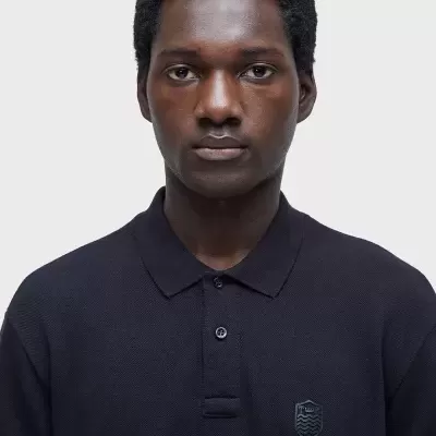 Homem com polo preta de malha com gola e emblema no peito