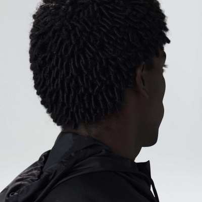 Homem de costas com cabelo encaracolado e casaco preto com capuz