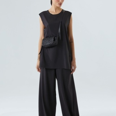 Mulher vestindo conjunto preto com bolsa pequena preta, em fundo cinza claro.