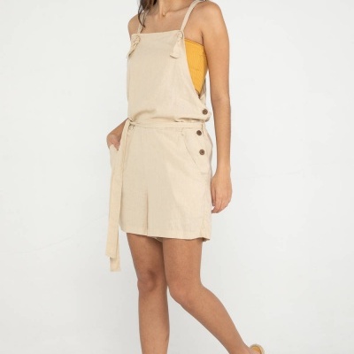 Macaquinho bege com alças finas usado por mulher sobre top amarelo e chinelos amarelos.