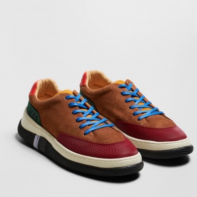 Sapatilhas casuais castanhas com detalhes vermelhos, verdes e atacadores azuis sobre fundo cinzento