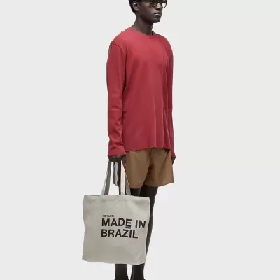 Homem com camisola vermelha, calções castanhos e saco de pano com texto 'SPLEARN MADE IN BRAZIL'