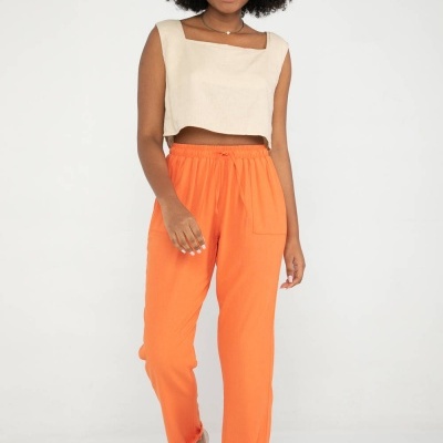 Mulher com top cropped bege e calças laranjas em fundo branco