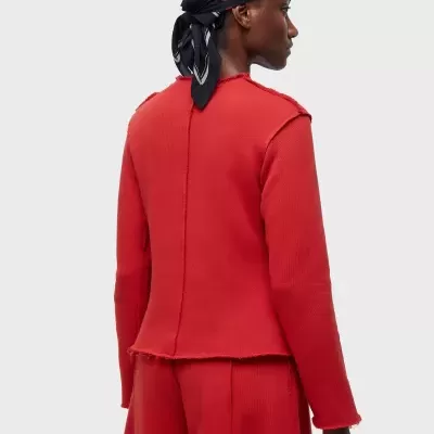 Mulher de perfil com blusa e calças vermelhas e lenço preto com flores na cabeça