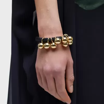 Pulseira preta com bolas douradas penduradas no pulso