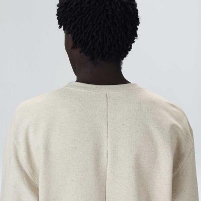 Pessoa vista de costas com camisola bege clara e cabelo encaracolado escuro