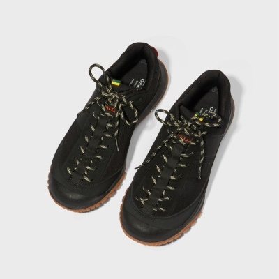 Par de sapatilhas pretas com sola castanha e atacadores com riscas brancas