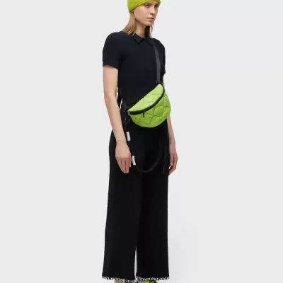 Mulher com roupa preta e acessórios verdes num fundo branco