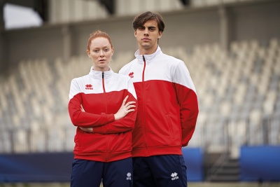 Dois modelos com casacos vermelhos e brancos e calças azuis em estádio