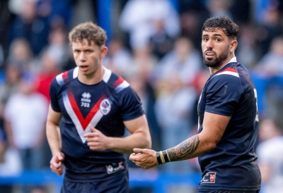 Dois jogadores de rugby com camisolas azul-escuras com padrão em V vermelho e branco em campo