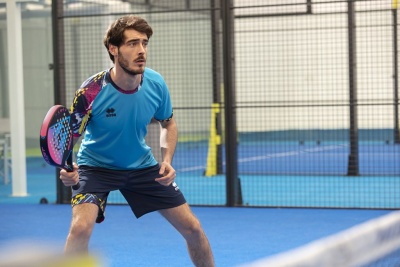 Homem a jogar padel com roupa desportiva azul e preta num campo de padel