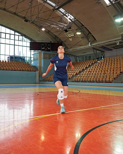 Homem a correr numa pista de basquetebol interior com t-shirt azul escura e joelheira branca