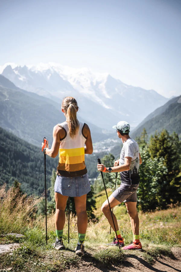 Duas pessoas a caminhar com bastões em paisagem montanhosa