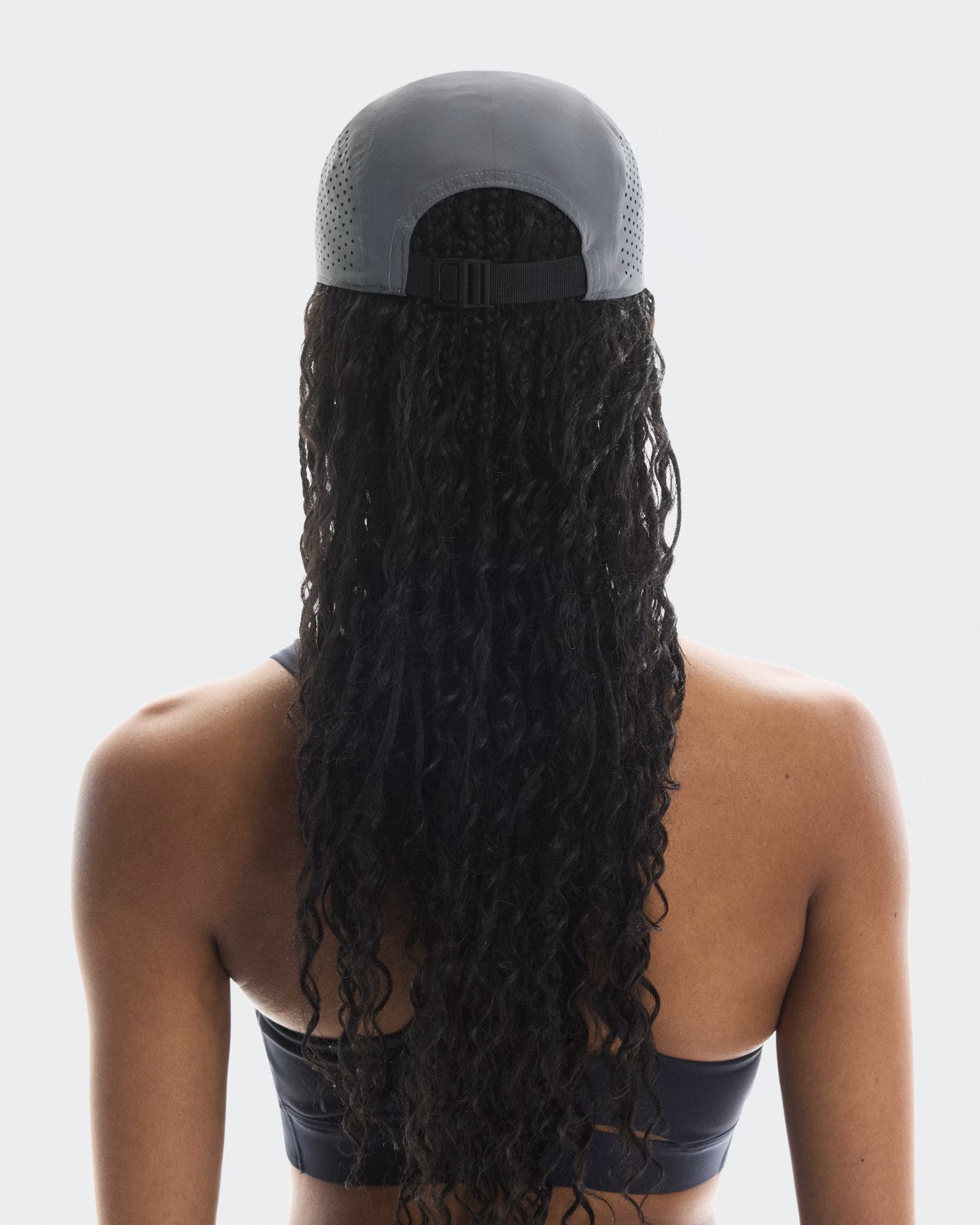 Mulher de costas com boné cinza e top desportivo preto