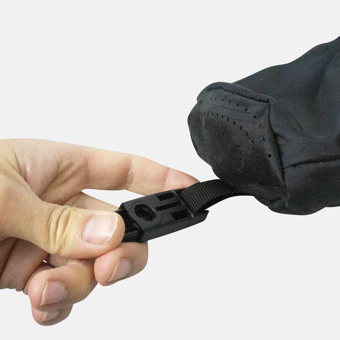 Fecho de mala ou saco preto com alça e tampa acolchoada com furos, segurada por uma mão.