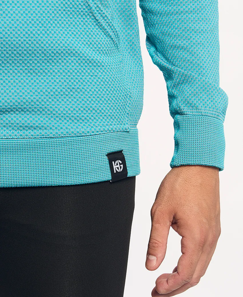 Detalhe de peça de vestuário azul turquesa com malha quadriculada e etiqueta preta com logótipo branco