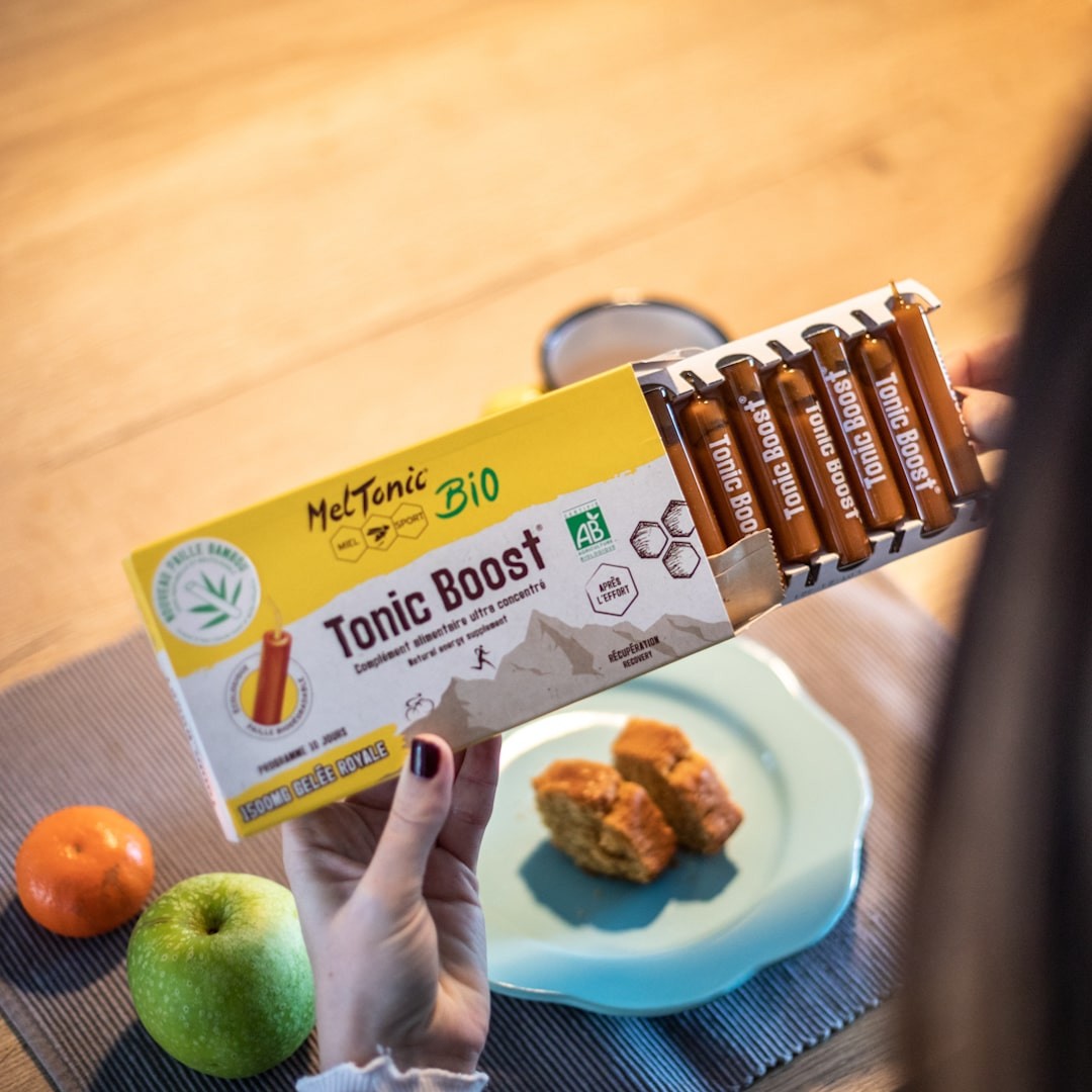 Caixa de Tonic Boost Bio MelTonic com sticks, maçã, tangerina, bolos e relógio numa mesa