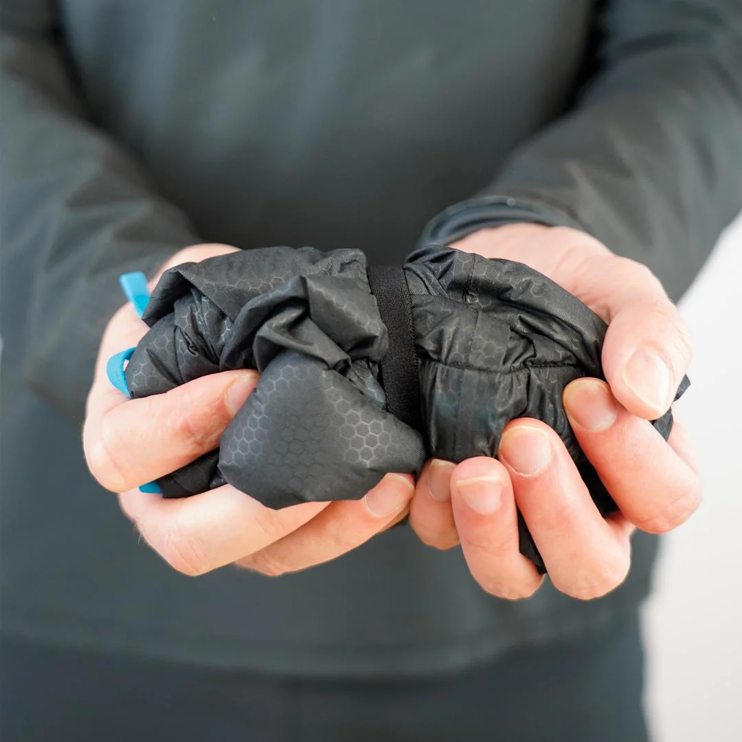 Casaco preto dobrado com padrão hexagonal segurado por mãos em fundo neutro