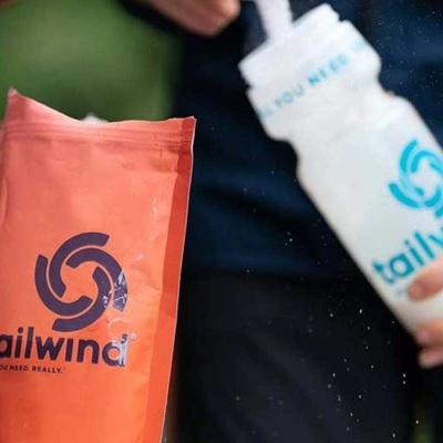 Saco de embalagem laranja com logo Tailwind em azul e garrafa branca com o mesmo logo