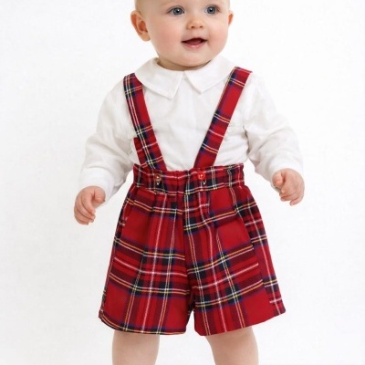 Bebé com camisa branca e calções xadrez vermelhos com suspensórios