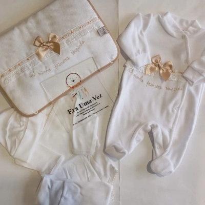 Conjunto de roupa branca de bebé com laço bege e bordado, acompanhado de fralda ou manta texturizada