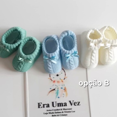 Sapatinhos de bebé em crochet verde, azul e branco com laços, sobre superfície branca com cartão informativo