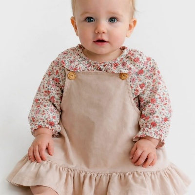 Bebé com vestido bege e blusa floral sentada sobre fundo branco