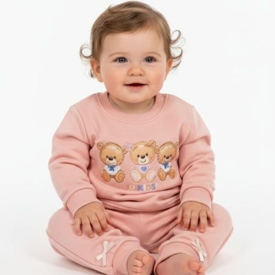 Bebé com fato de treino rosa com ursinhos bordados e laços nas calças sentado no chão