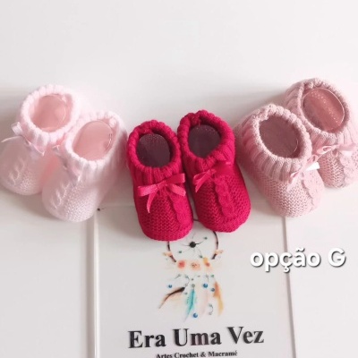 Três pares de sapatinhos de crochet para bebé em rosa claro e vermelho sobre placa com texto Era Uma Vez.
